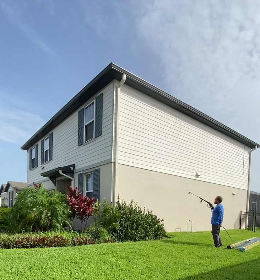 Brett Horton, owner of One Touch Softwash & paver Sealing, using a power washing wand to clean the exterior wall of a residence.