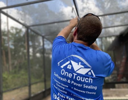 Brett Horton, owner of One Touch Softwash & Paver Sealing using a power washing sprayer to clean a pool enclosure.